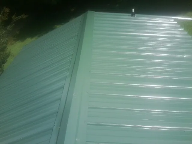 New green metal panels meeting at the ridge of a roof — Flat Roof Repair work by our crew in Benton Harbor