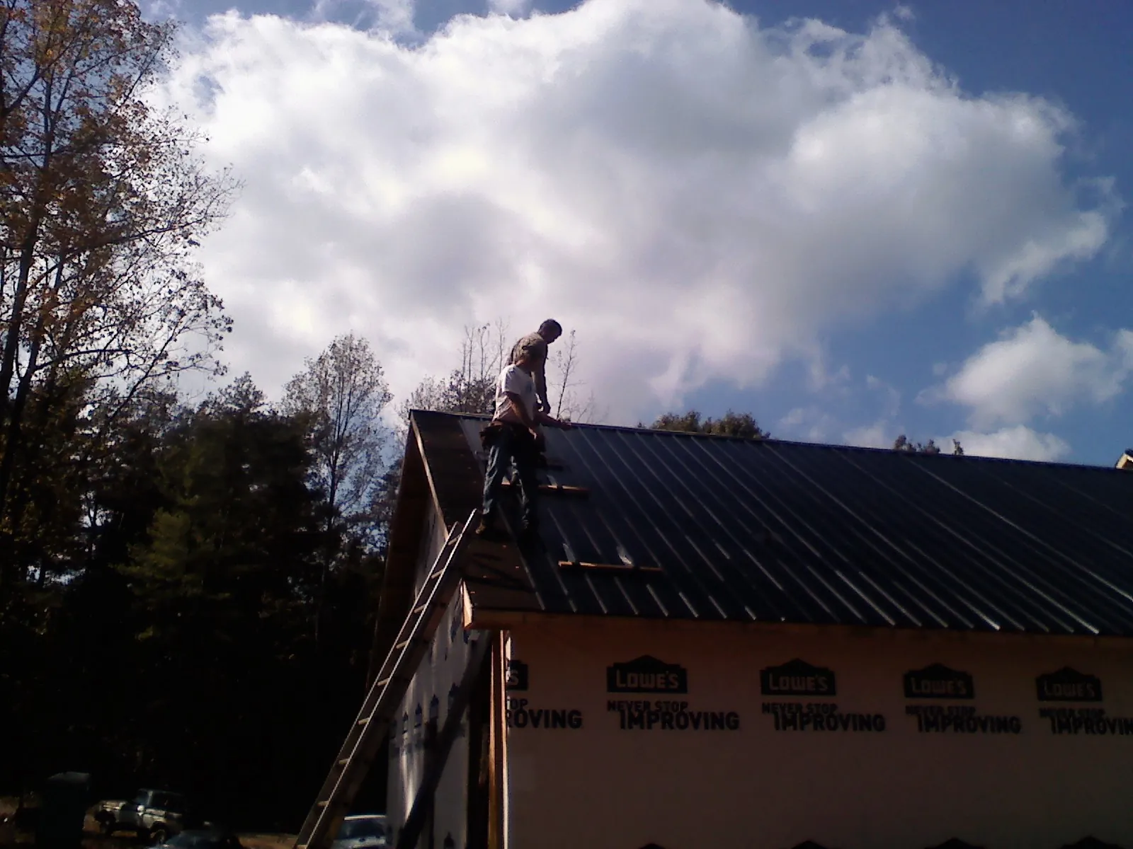 Roofer fastening dark metal panels high against a cloudy sky, from a Roof Inspection job in Benton Harbor
