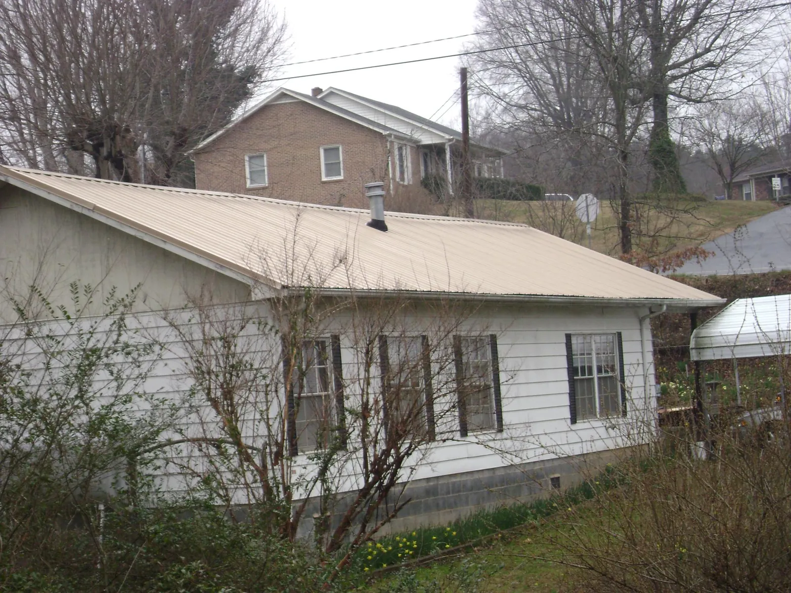 Tan metal roof on a white sided house set into a hillside — Commercial Roofing by Roofing Brothers in Benton Harbor