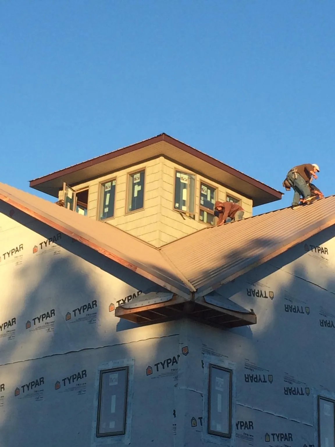 Roofers working around a rooftop cupola on a new metal roof at sunset — Roof Waterproofing in Benton Harbor by Roofing Brothers